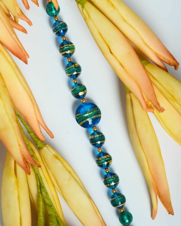 Close-up of a Murano necklace with vibrant blue beads featuring gold accents, displayed on a decorative surface